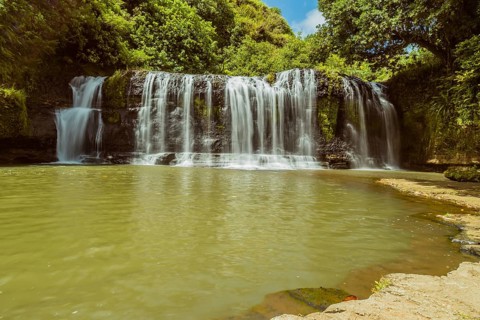 Landscape of a waterfall taken with ND filter with trees and blue sky in the background and water