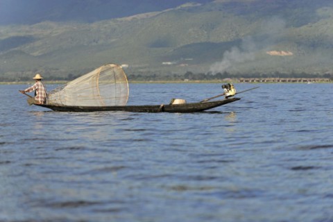 Fisherman enjoying the sun rays while working, surrounded by a mountain landscape, Inle Lake,