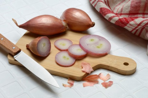 Sliced shallots on a wooden board with a knife, Allium cepa