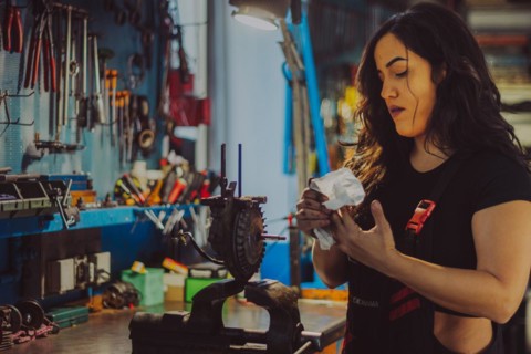 A female mechanic wearing overall in a workshop is carefully cleaning motorcycle parts, a complete