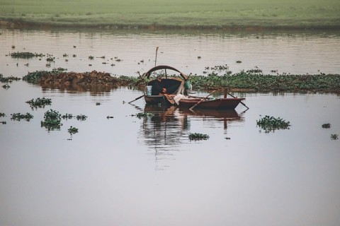 A serene scene with a lone boat on a calm river amidst greenery, Ninh Binh, Vietnam, Asia