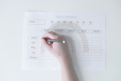 Diabetes log, daily log of food and insulin administration, food log, hand of a child holding a pen