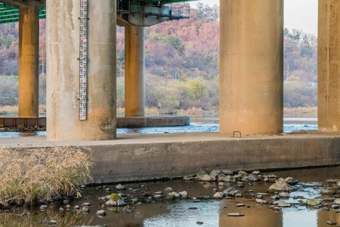 Pillars of a bridge over a river showing a water level gauge, with fall foliage around, in South