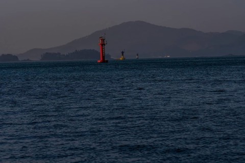 Three small light houses in a harbor with small mountains shrouded in fog and mist in the