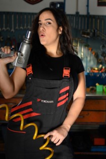 Playful hispanic female mechanic making a gesture in the workshop, a complete tool panel in