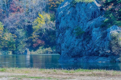 Rock faces with autumnal trees reflected in a calm lake creating a peaceful landscape, in South