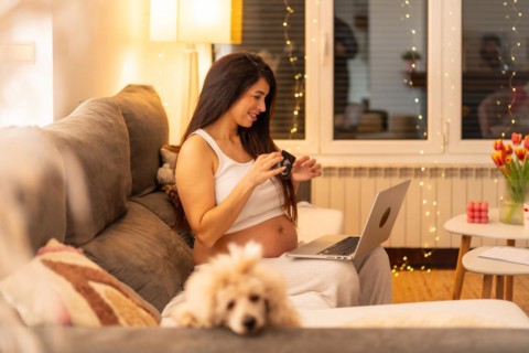 Pregnant woman using laptop sitting on the sofa to do a video call and showing a ultrasound from