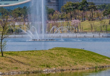 Fountain with water jets in a lake at a park with city skyline in background, in South Korea