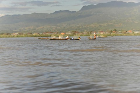 Fishing boats glide across the water with mountains in the background, Inle Lake, Myanmar, Asia