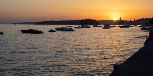 Boats anchoring in a bay, silhouette of a church tower, sunset over Rab, panoramic view, town of