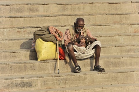 Old man sitting alone on the steps and looking at an object, Varanasi, Uttar Pradesh, India, Asia