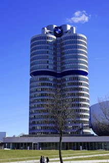 BMW main building, known as the 'four-cylinder', against a clear sky with trees in the foreground,