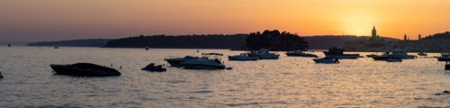 Boats anchoring in a bay, silhouette of a church tower, sunset over Rab, panoramic view, town of