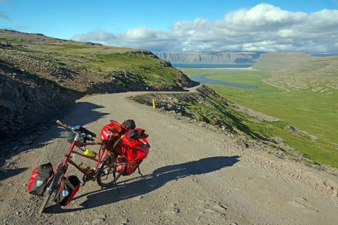 Packed bike standing on a gravelled track leading out into a wide valley, Adventure travel, Cycle