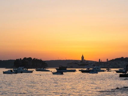 Boats anchoring in a bay, silhouette of church towers, evening mood after sunset over Rab, town of