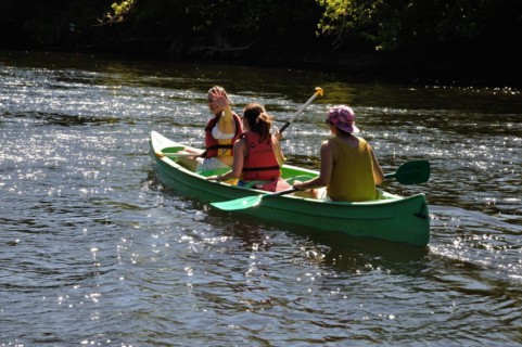 Two people paddling a green canoe on a sunlit river surrounded by nature, LA ROQUE GAGEAC FRANCE,