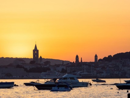 Boats anchoring in a bay, silhouette of church towers, evening mood after sunset over Rab, town of