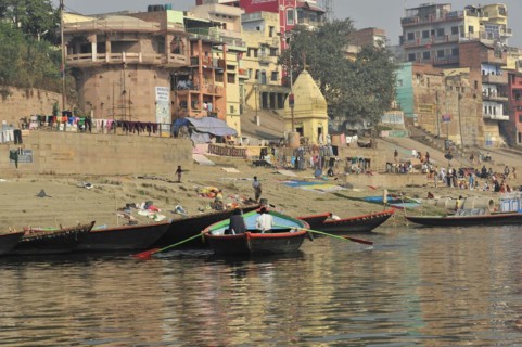 Boats at the edge of a river with people walking along the bank, Varanasi, Uttar Pradesh, India,