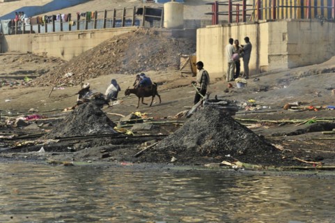 Busy riverbank full of people and animals, smoke and pollution emphasise the daily drama, Varanasi,