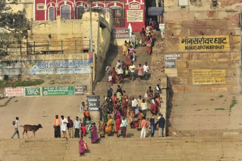 A group of people in traditional dress gather on a riverbank with yoga signs, Varanasi, Uttar