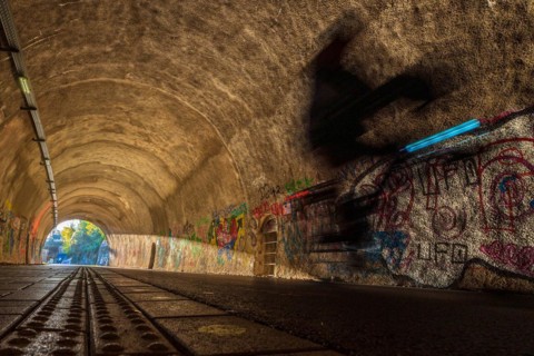 Blurred cyclist in a tunnel whose walls are covered with colourful graffiti, Nordbahntrasse,