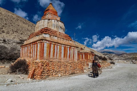 Woman with her horse, colourfully painted Buddhist stupa in front of mountain landscape, erosion