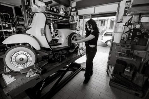 Woman mechanic working on repairing a white moped italian vintage scooter, surrounded by tools in a