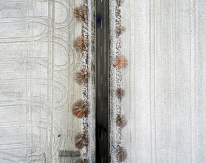 An aerial view shows an avenue with trees leading through snow-covered fields on which tyre tracks
