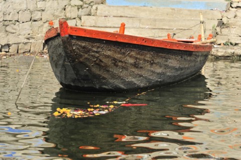 A single boat floats with a flower offering on the calm waters of a river in India, Varanasi, Uttar