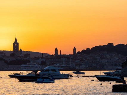 Boats anchoring in a bay, silhouette of church towers, evening mood after sunset over Rab, town of