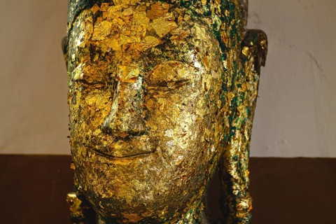 Close-up of a Buddha head adorned with gold leaf, showing texture and age