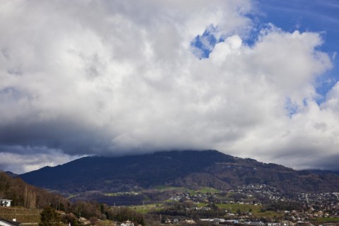 Mighty white spring clouds move under a blue sky over a wooded hill near Jongny, Jongny,