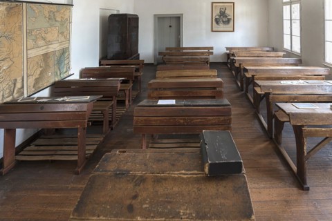 Classroom with school desks and teacher's desk from the 19th century, behind a photograph of Tsar
