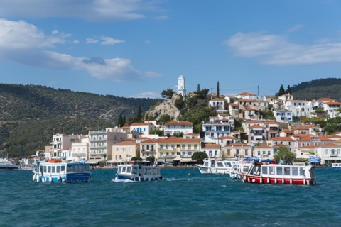 View of a lively harbour with colourful houses in front of a hill under a blue sky with clouds,