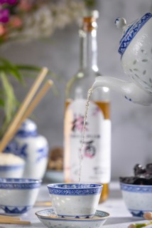 Pouring tea, Asian tea set with blue patterns, a bottle of China plum wine in the background, dried
