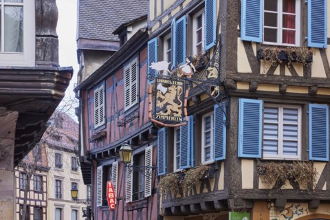 Pastel-coloured facades of historic half-timbered houses with white windows and blue-green shutters