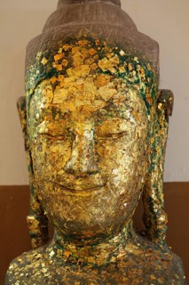 Weathered Buddha head covered with gold flakes, displaying a serene expression