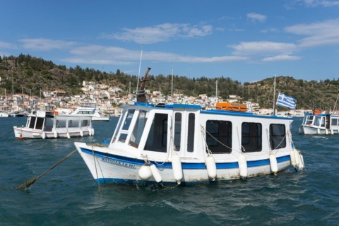 A small boat sways on the clear water of a picturesque harbour with a city view in the background,