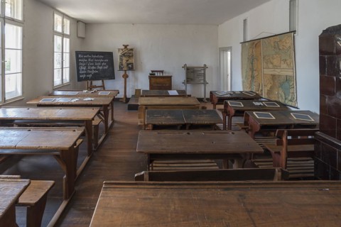 School desks, chalkboard and map, on the right a tiled stove in a classroom from the 19th century,