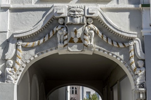 Decorative figures above gateway in Art Nouveau style, naked boys with garland, grim male face,