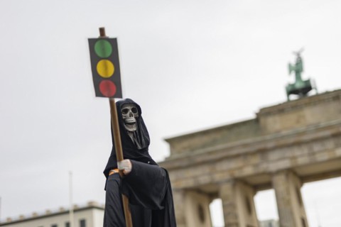 The figure of a grim reaper (skeleton) with a traffic light as a sign, the Brandenburg Gate in the