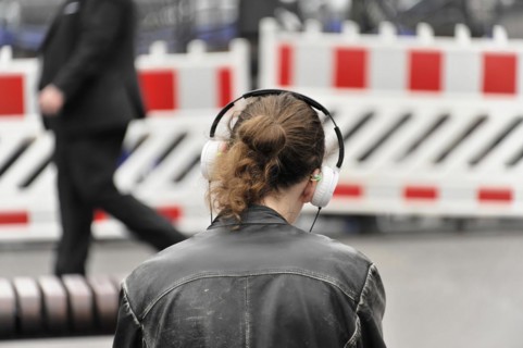 A person with headphones stands in front of a roadblock, taken from behind, Hamburg, Hanseatic City