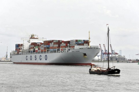A large container ship next to a small sailing boat in a cloudy harbour, Hamburg, Hanseatic City of