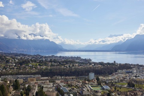 View of Vevey and Lake Geneva with cloudy, misty mountains in the background from Jongny,