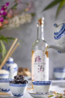 Pouring tea, Asian tea set with blue patterns, a bottle of China plum wine in the background, dried