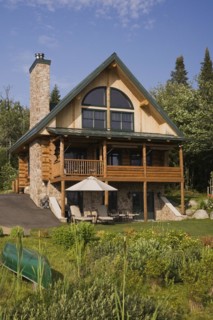 Handcrafted two story spruce log home cabin with fieldstone chimney, green sheet metal roof and