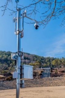 Wi-fi, CCTV with 5 G transmitters on chrome pole in from of evergreen tree in public park with lake