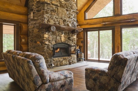 Upholstered sofas with lit fieldstone and porous rock fireplace in living room inside handcrafted