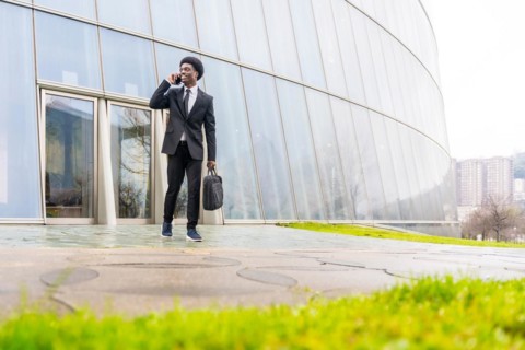 African businessman talking to the mobile holding computer bag in the street in a financial