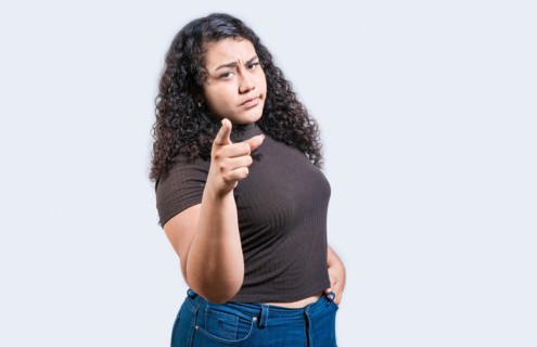 Serious young woman pointing at the camera, isolated. Young girl pointing at you frowning isolated